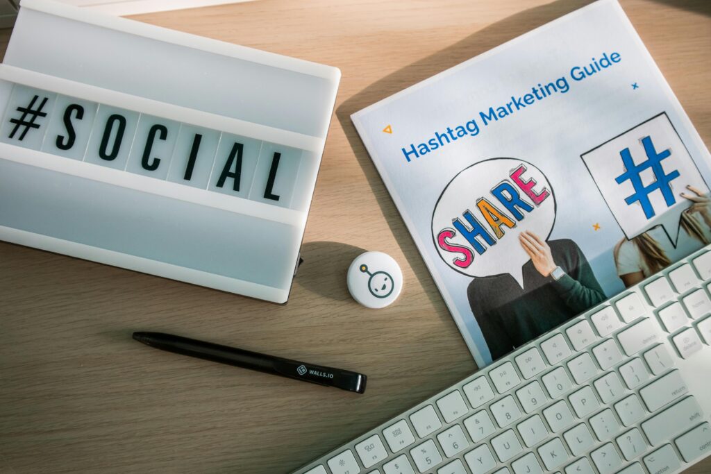 Social media marketing workspace with a laptop displaying the word social, a hashtag marketing guide, and a keyboard on a desk.